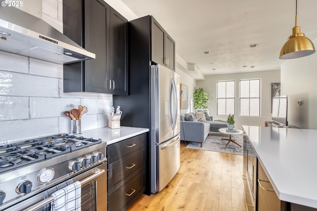 kitchen with open floor plan, light countertops, appliances with stainless steel finishes, wall chimney exhaust hood, and decorative light fixtures