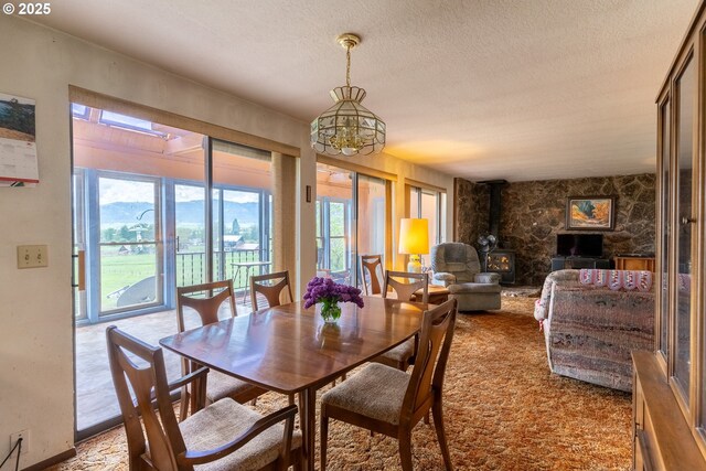 dining area featuring a chandelier, a wood stove, a textured ceiling, and carpet
