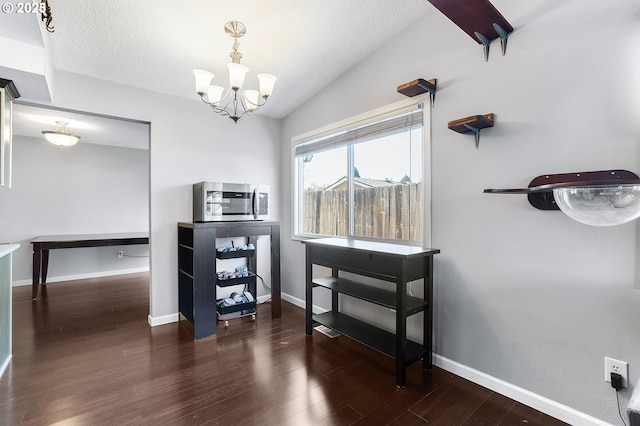 interior space with an inviting chandelier, vaulted ceiling, wood finished floors, and baseboards