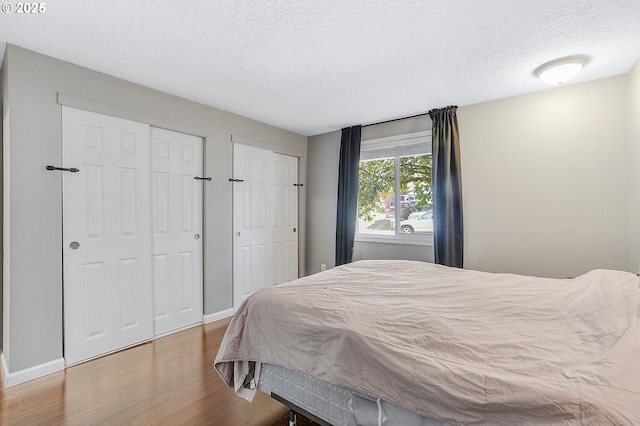 bedroom with baseboards, two closets, wood finished floors, and a textured ceiling