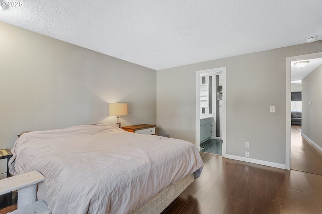 bedroom featuring baseboards, wood-type flooring, a textured ceiling, and ensuite bath