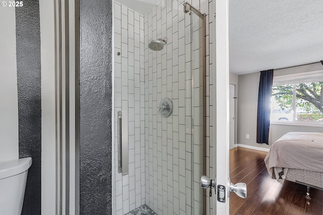 full bath with baseboards, toilet, a stall shower, wood finished floors, and a textured ceiling