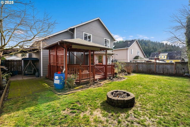 back of property with a yard, a deck, and a fire pit