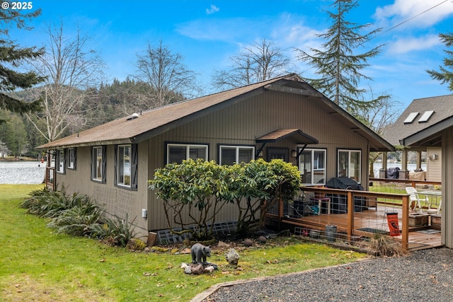 view of front of property with a deck, a shingled roof, and a front yard