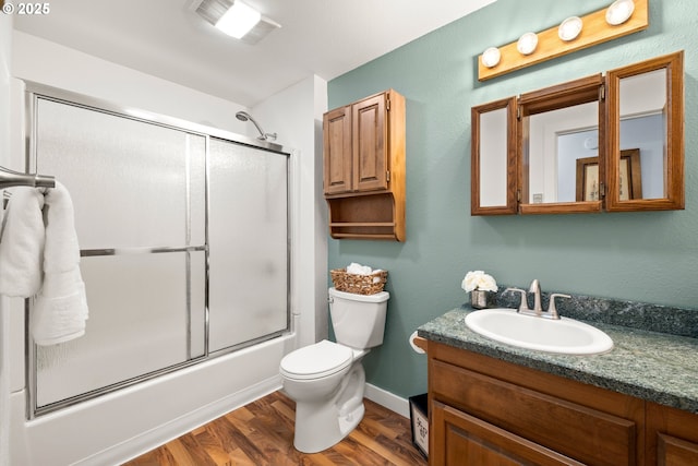 bathroom with visible vents, toilet, wood finished floors, combined bath / shower with glass door, and vanity