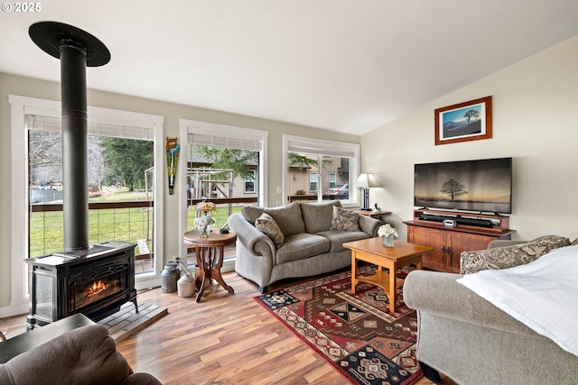 living room with a wood stove, vaulted ceiling, and wood finished floors