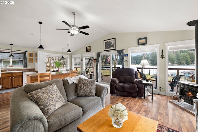 living area with lofted ceiling, ceiling fan, light wood finished floors, and a wood stove