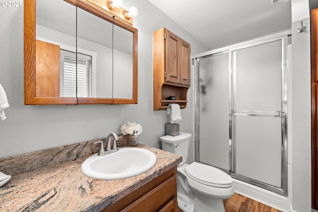 bathroom featuring wood finished floors, a shower stall, toilet, and vanity