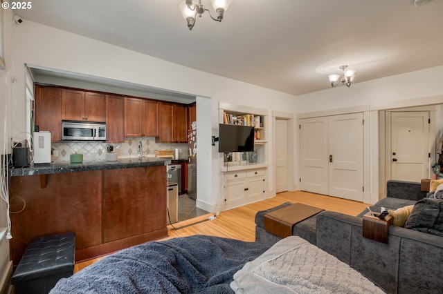 interior space with light wood-type flooring, a kitchen bar, stainless steel microwave, open floor plan, and backsplash