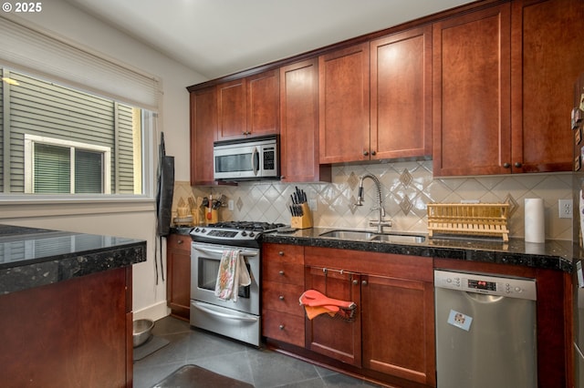 kitchen featuring dark tile patterned floors, a sink, backsplash, stainless steel appliances, and dark stone counters