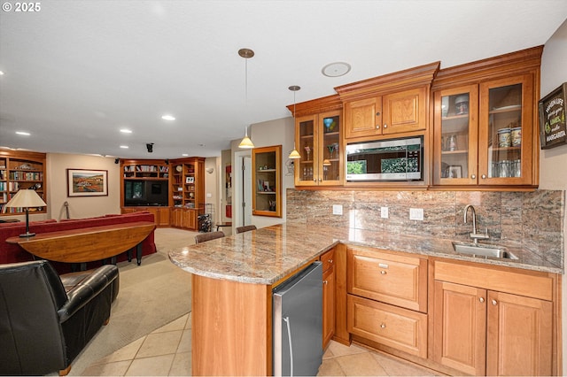 kitchen with a sink, open floor plan, stainless steel microwave, a peninsula, and brown cabinetry