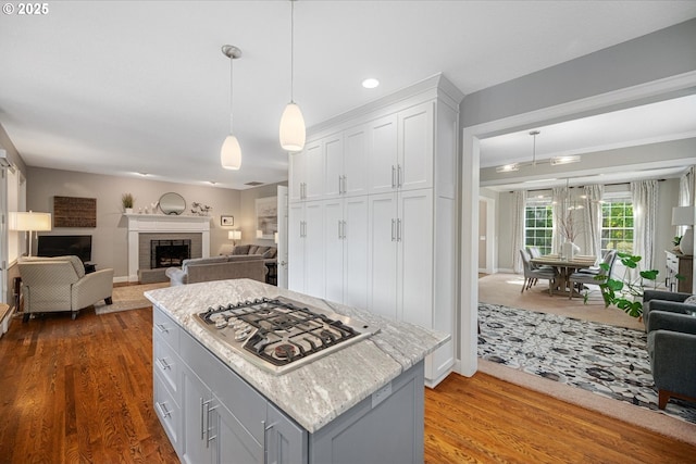 kitchen with stainless steel gas stovetop, open floor plan, wood finished floors, white cabinetry, and pendant lighting