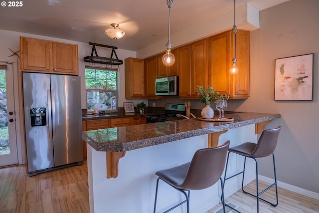 9235 NW Germantown Rd, Portland, OR 97231 - kitchen featuring appliances with stainless steel finishes, light wood-style flooring, brown cabinets, a peninsula, and a kitchen bar