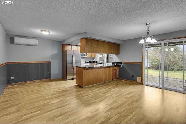 kitchen with dark countertops, an AC wall unit, brown cabinets, a peninsula, and stainless steel appliances