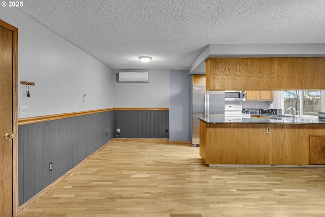 kitchen featuring stainless steel appliances, a peninsula, an AC wall unit, and light wood-style flooring