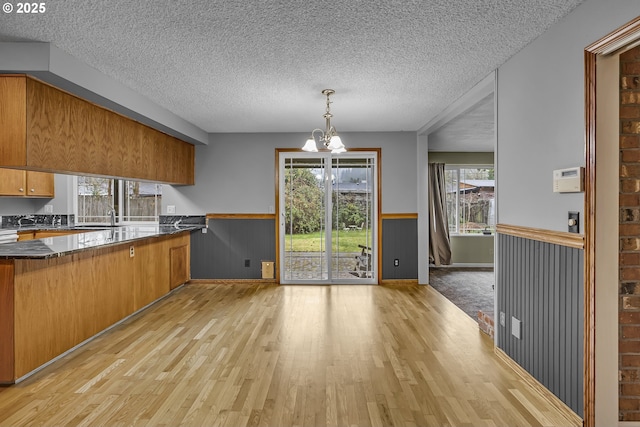 kitchen featuring wainscoting, light wood-style floors, a chandelier, and brown cabinetry