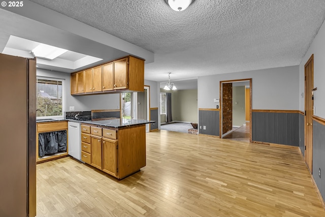 kitchen featuring brown cabinetry, dishwashing machine, wainscoting, and freestanding refrigerator