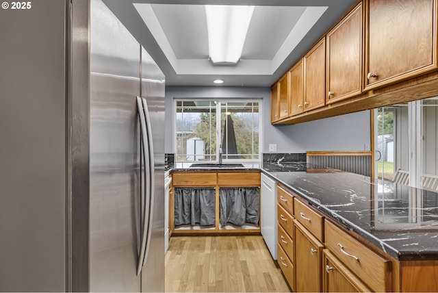 kitchen with brown cabinetry, white dishwasher, freestanding refrigerator, and light wood-type flooring