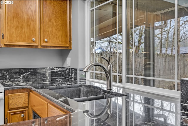 kitchen featuring brown cabinetry, dark stone counters, and a sink