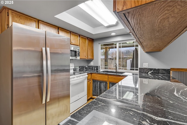 kitchen with a sink, dark stone countertops, brown cabinets, and stainless steel appliances