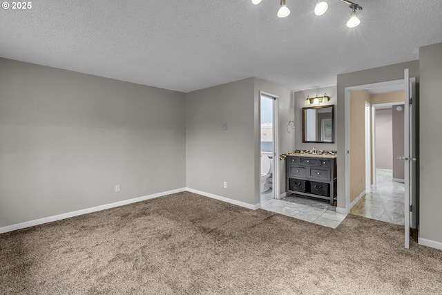 unfurnished living room featuring baseboards, carpet floors, a textured ceiling, and a sink