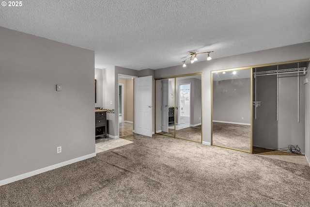 unfurnished bedroom with carpet flooring, a textured ceiling, two closets, and baseboards