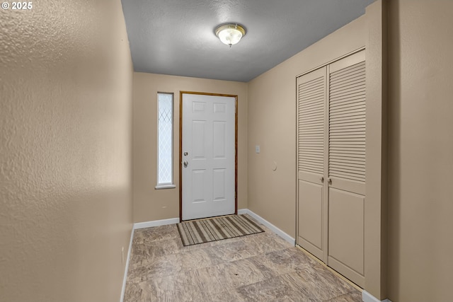 foyer featuring a textured wall and baseboards