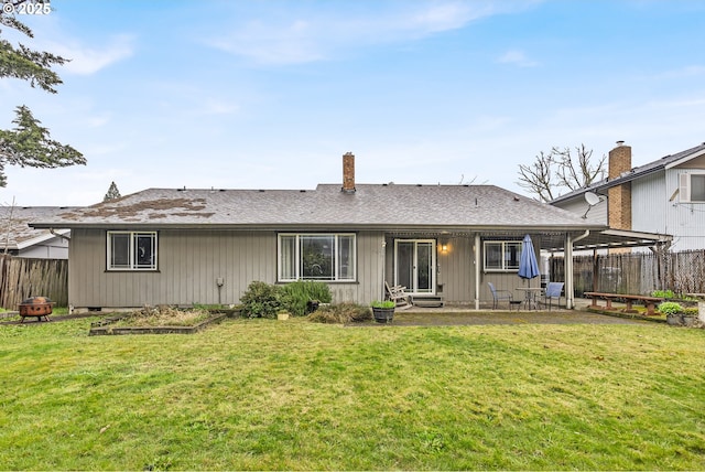 back of property with a lawn, a shingled roof, a patio, and fence