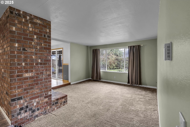 unfurnished living room with carpet floors, a textured ceiling, and baseboards