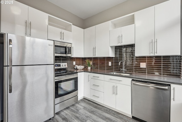 kitchen with stainless steel appliances, white cabinetry, sink, and backsplash