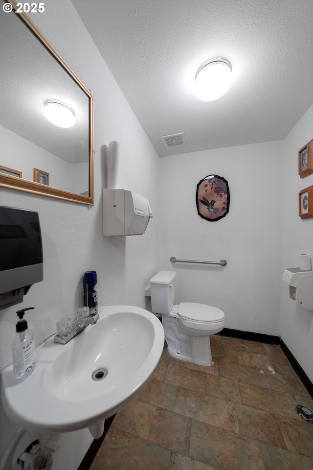 115 8th St, Winchester Bay, OR 97467 - bathroom with stone tile floors, a sink, toilet, baseboards, and a textured ceiling