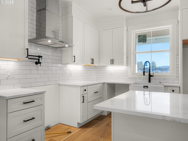 kitchen with sink, white cabinetry, light hardwood / wood-style floors, decorative backsplash, and wall chimney range hood