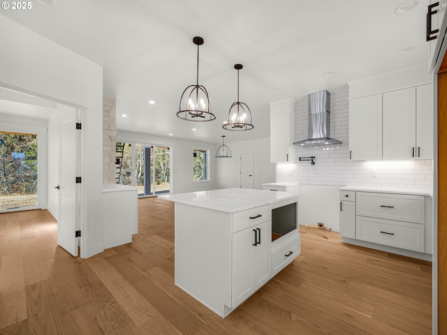 kitchen featuring white cabinets, a center island, wall chimney exhaust hood, and light wood-type flooring