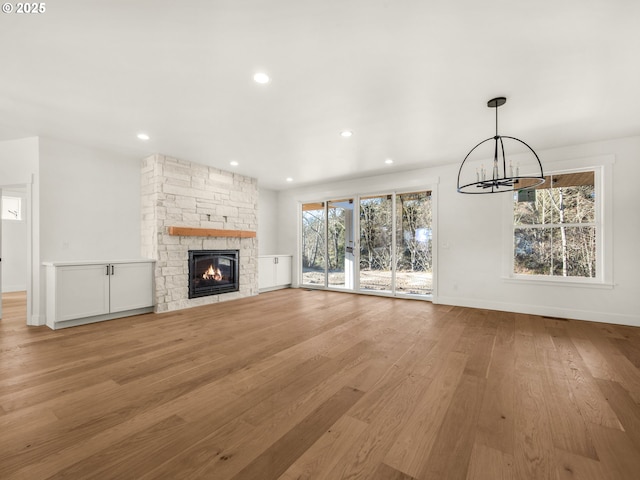 unfurnished living room featuring an inviting chandelier, a fireplace, and light hardwood / wood-style floors