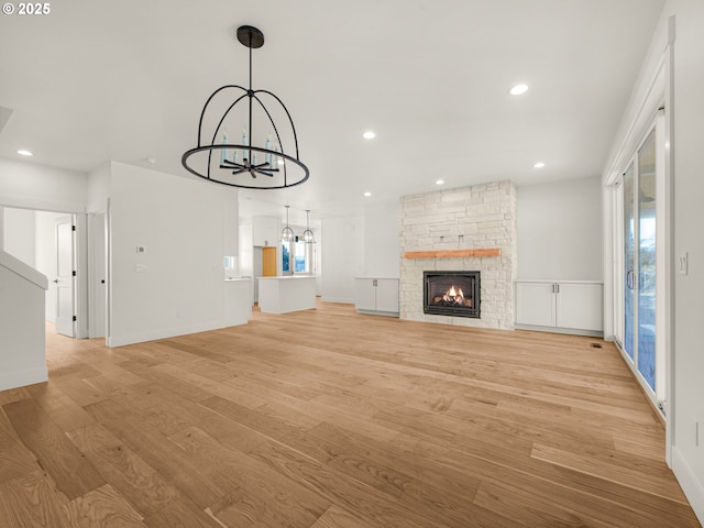 unfurnished living room featuring a fireplace, a chandelier, and light hardwood / wood-style flooring