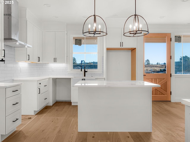 kitchen featuring a kitchen island, pendant lighting, wall chimney range hood, and white cabinets