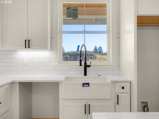 interior details featuring backsplash, light stone countertops, sink, and white cabinets