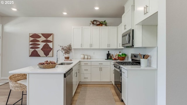 6558 SE Nasha St, Hillsboro, OR 97123 - kitchen with a sink, stainless steel appliances, a peninsula, light wood-style flooring, and a kitchen breakfast bar