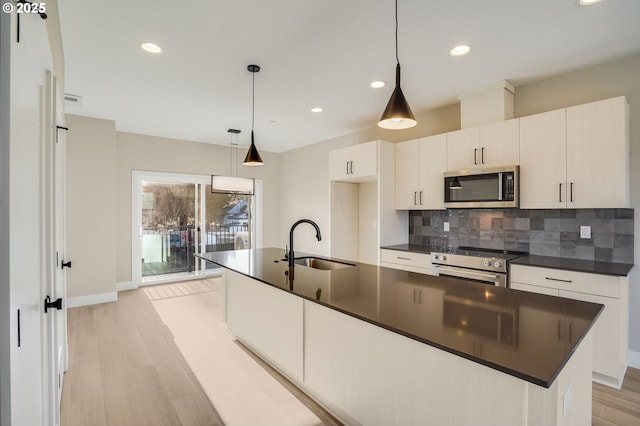kitchen featuring appliances with stainless steel finishes, a sink, dark countertops, light wood-style flooring, and recessed lighting