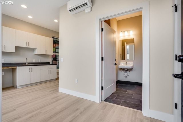 kitchen featuring an AC wall unit, dark countertops, a sink, light wood-style flooring, and recessed lighting