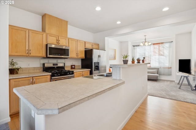 kitchen with appliances with stainless steel finishes, a notable chandelier, light hardwood / wood-style floors, a kitchen island, and decorative light fixtures