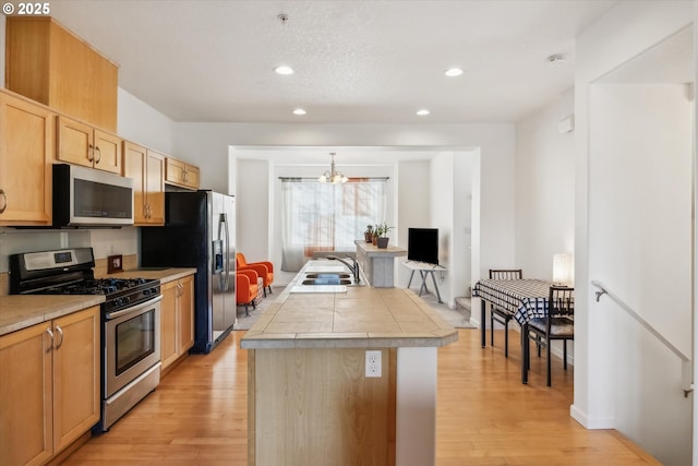 kitchen with an inviting chandelier, stainless steel appliances, a center island, light hardwood / wood-style floors, and decorative light fixtures