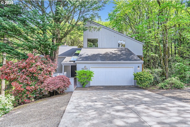 mid-century home with concrete driveway, an attached garage, and a shingled roof