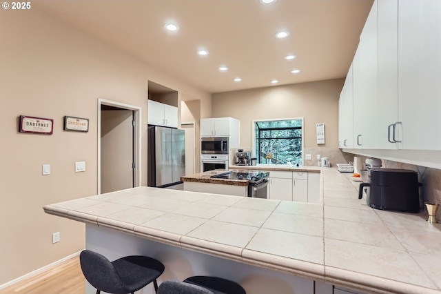 kitchen featuring a peninsula, a breakfast bar area, recessed lighting, white cabinets, and appliances with stainless steel finishes