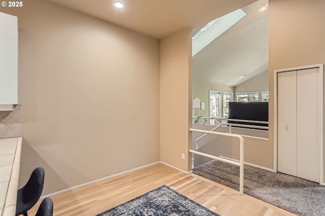 interior space featuring vaulted ceiling with skylight, baseboards, recessed lighting, and wood finished floors