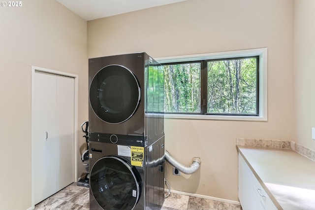 clothes washing area featuring baseboards, cabinet space, and stacked washing maching and dryer
