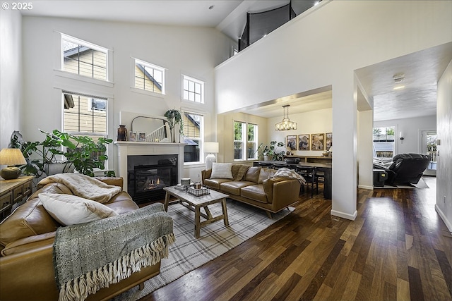 living area featuring a towering ceiling, a glass covered fireplace, wood finished floors, and a wealth of natural light