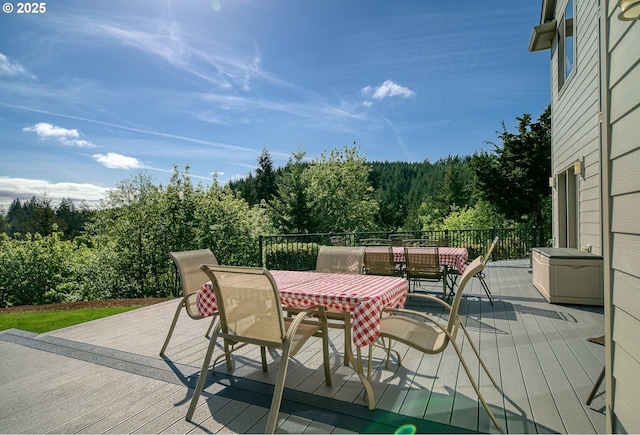 wooden deck with a view of trees and outdoor dining space