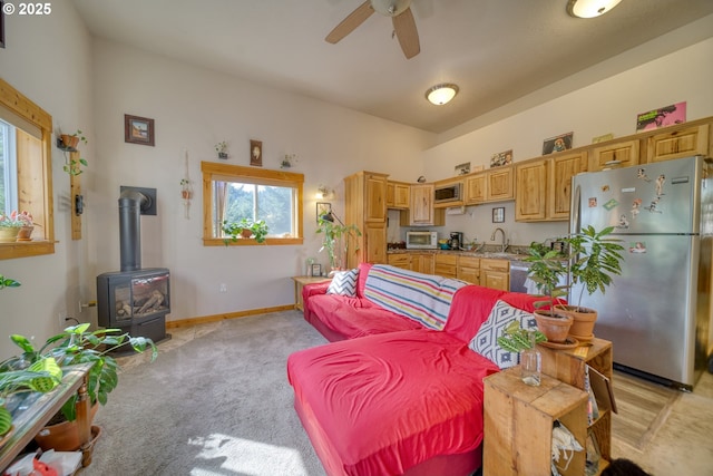 living room featuring baseboards, a wood stove, ceiling fan, and light carpet
