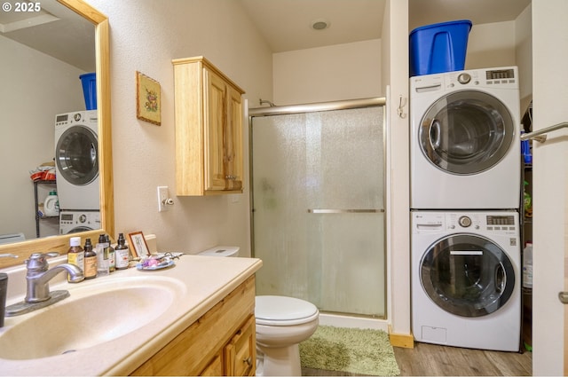 full bath featuring stacked washer and dryer, a shower stall, wood finished floors, vanity, and toilet